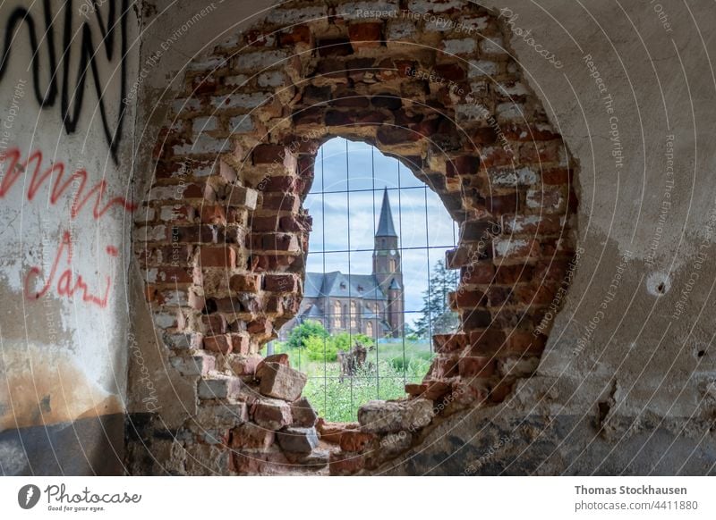 church in Manheim, a village that is being demolished for open-cast lignite mining, view through a hole in a brick wall abandoned architecture boarded up house