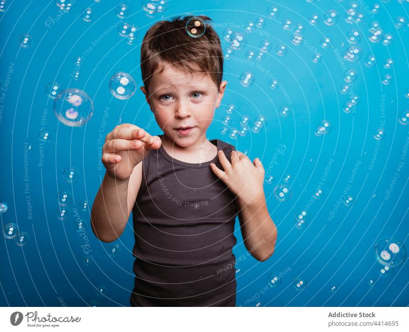 Shocked child showing touching gesture in studio with soap bubbles index finger forefinger shock astonish amazed boy kid surprise childhood face expression wow