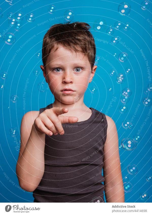 Shocked child showing touching gesture in studio with soap bubbles index finger forefinger shock astonish amazed boy kid surprise childhood face expression wow