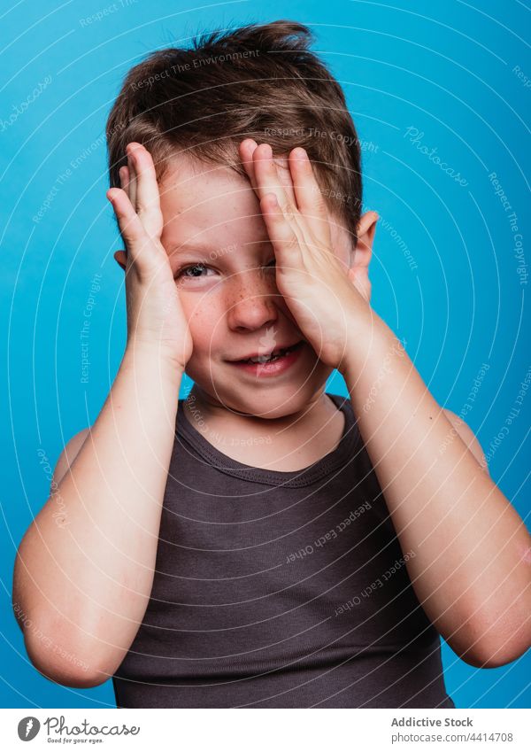 Charming kid covering eye and looking at camera child cover eye hide smile boy cheerful shy modest happy style adorable cute studio childhood glad bright vivid