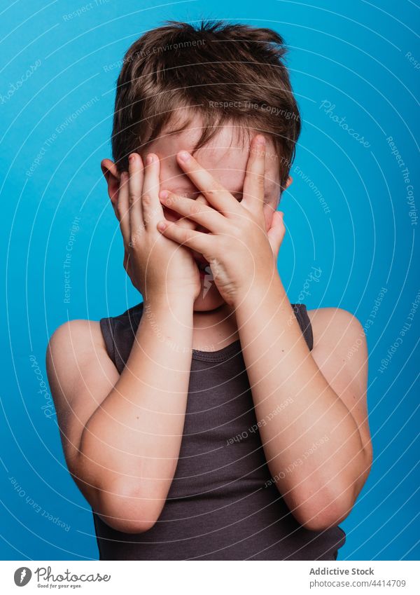 Charming kid covering face on blue background child cover face hide boy cheerful shy modest happy style adorable cute studio hand childhood glad bright vivid