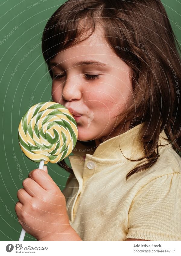 Cheerful girl with spiral candy on green background lick lollipop swirl sweet funny child kid dessert cute adorable happy tasty delicious stick treat