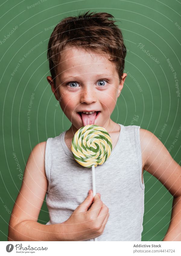Funny boy licking sweet lollipop on stick in studio child tongue candy make face delicious having fun funny kid tasty treat yummy confectionery sugar childhood