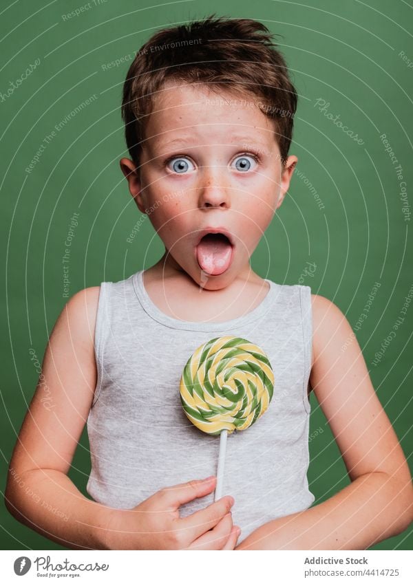 Cheerful child with lollipop on stick on green background tongue out swirl thumb up like gesture sign cheerful boy happy positive childhood smile joy studio