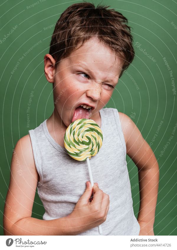 Funny boy licking sweet lollipop on stick in studio child candy grimace make face delicious having fun funny kid tasty treat yummy confectionery sugar childhood