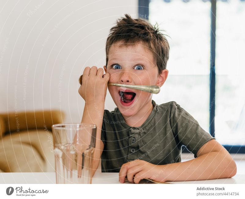 Funny boy playing with spoon in kitchen having fun mustache entertain funny child kid childhood cute table home adorable happy expressive smile cheerful sit
