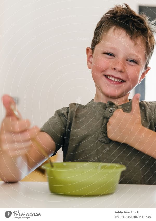 Cheerful kid eating lunch an showing thumb up child like gesture good food boy smile happy cheerful kitchen home tasty childhood delicious cute sweet delight