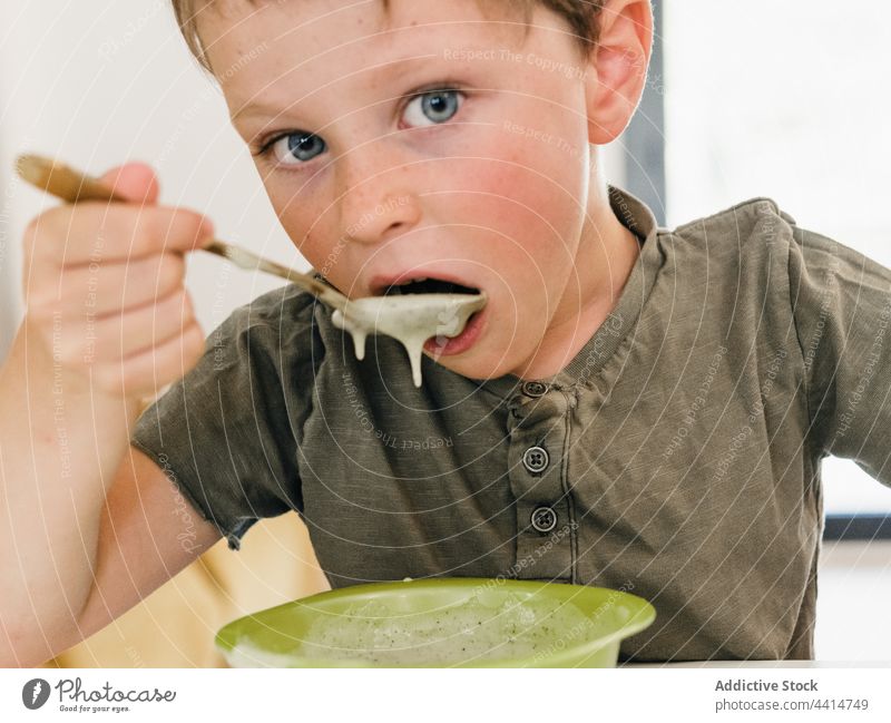 Funny kid with dirty mouth having lunch at home child eat food boy meal funny bowl table sit childhood messy cream soup puree dish serve cuisine tasty cute