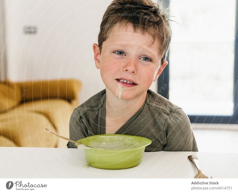 Sad kid with dirty mouth having lunch at home child disgusted sad eat food boy meal bowl table sit childhood messy cream soup puree dish serve cuisine tasty