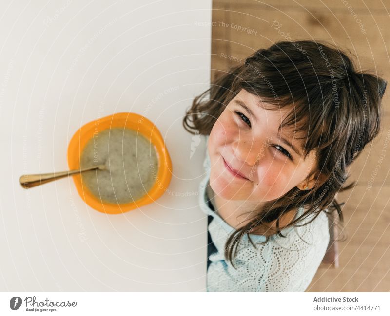 Happy girl sitting at table with soup during lunch child kid kitchen food meal bowl cream puree cheerful childhood cute domestic smile spoon happy joy glad