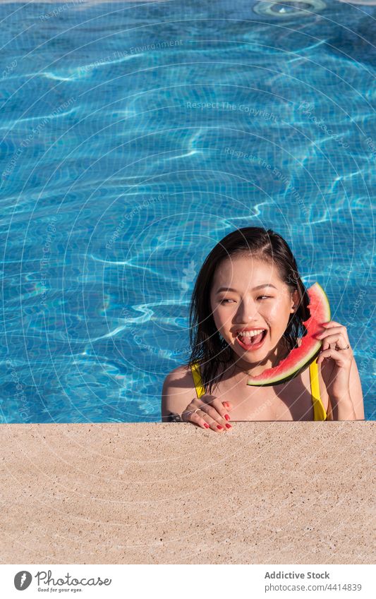 Asian woman having fun with watermelon as phone in swimming pool dial cheerful playful slice summer female ethnic asian happy positive smile talk speak pretend