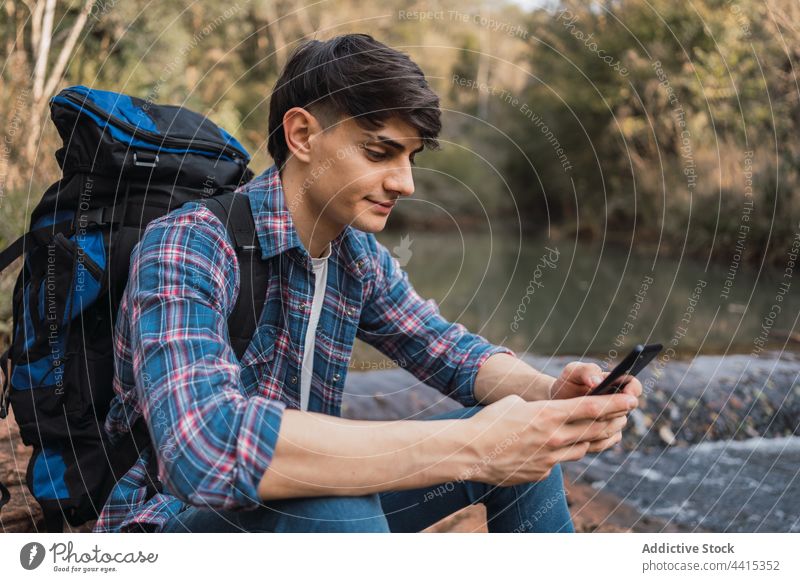 Smiling traveling man using smartphone during hike traveler browsing backpack trekking forest hiker male nature gadget smile content device backpacker adventure