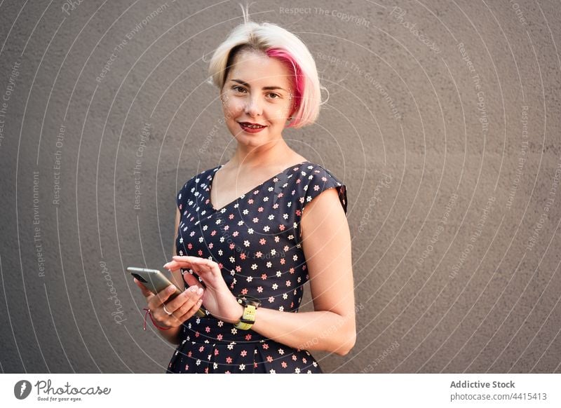 Content alternative woman using smartphone in city message informal style cheerful browsing female subculture fancy dress short hair dyed hair gadget smile