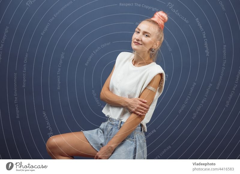 Young hipster woman with band aid after coronavirus Covid-19 vaccine injection. Covid vaccination concept, plain color background covid arm young showing