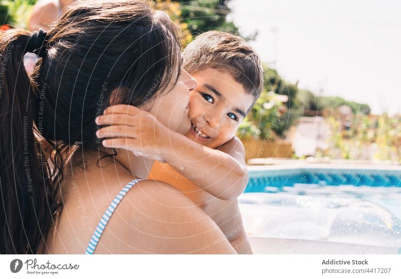 Young woman with son in swimming pool smiling summer water garden together vacation mother tree nature boy parent motherhood poolside kid childhood activity