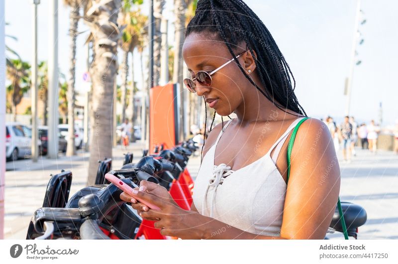 Black woman using smartphone for renting bicycle in city app share bike cellphone female ethnic black african american barceloneta barcelona spain street urban