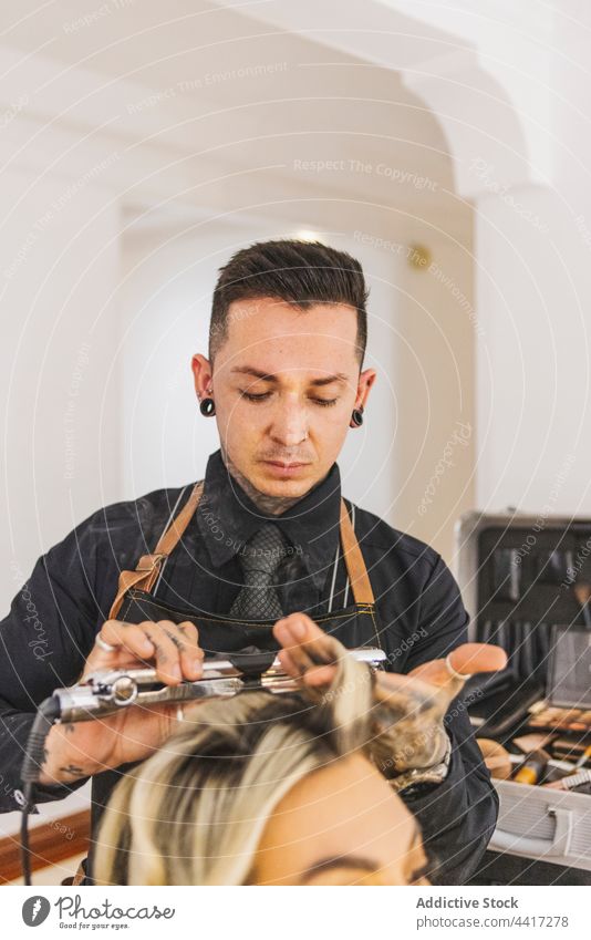 Male hairdresser curling hair of woman client salon iron professional hairstyle service customer job hairstylist hairdo procedure work specialist master blond