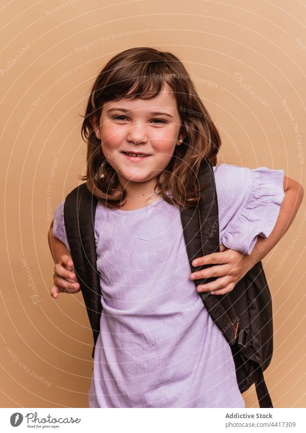 Charming girl with backpack on brown background schoolgirl duck face child studio make face schoolchild pupil kid appearance cute adorable schoolkid funny style