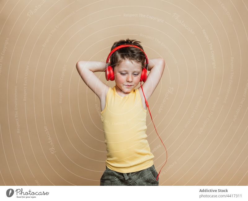 Child listening to music in headphones in studio boy child preteen enjoy carefree red color song kid audio modern device gadget tune using entertain sound