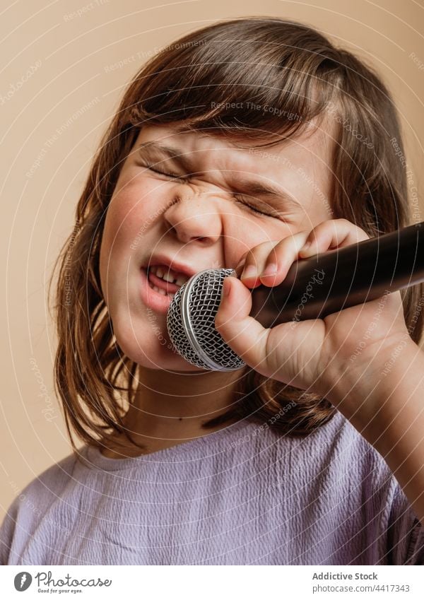 Funny child singing in mic in studio microphone girl funny make face comic grimace song entertain face expression cool singer style trendy music contemporary