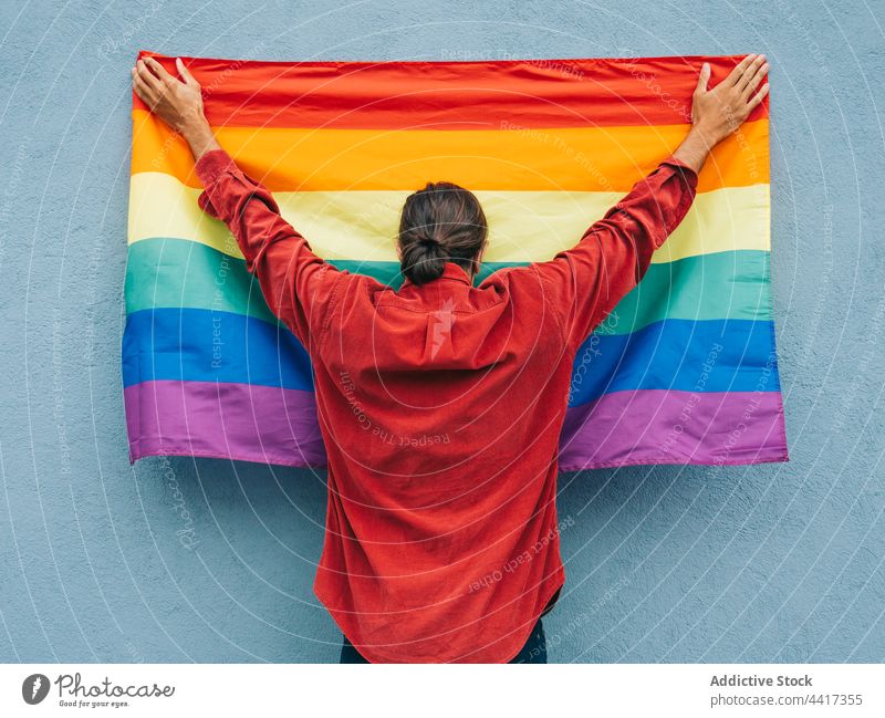 Unrecognizable gay man with rainbow flag near wall in city homosexual lgbt colorful pride lgbtq male equal tolerance street arms raised hand raised hand up
