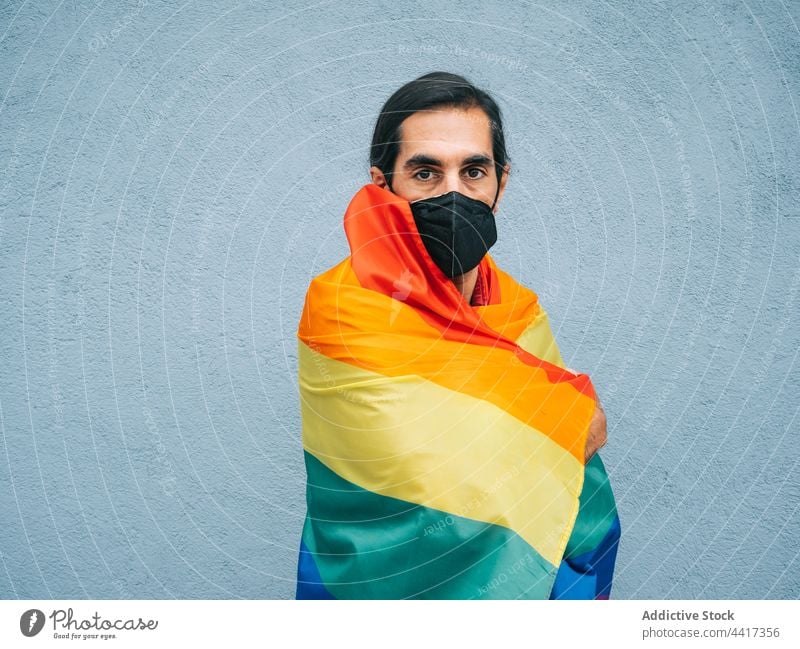 Homosexual ethnic man in mask wrapped in LGBT flag in city gay rainbow coronavirus new normal homosexual male lgbtq covid19 right respect pride equal tolerance