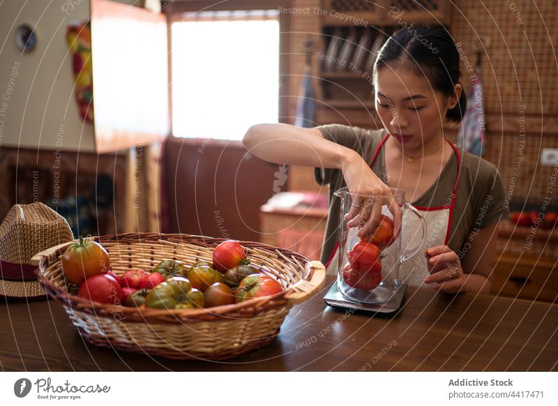 Asian woman weighing tomatoes on kitchen scale cook housewife food prepare vegetable female ethnic asian home glass jug pitcher healthy cuisine fresh culinary