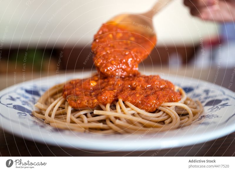 Crop cook adding marinara sauce on spaghetti tomato chef lunch pasta meal tasty food delicious dish cuisine pour culinary table serve plate appetizing