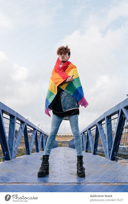 Gay man with LGBT flag on bridge homosexual rainbow lgbt gay pride freedom city style male trendy stand arms raised hand raised lgbtq tolerance equal confident