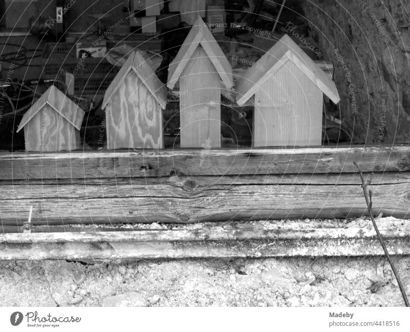 Rustic small wooden houses with pointed gables for children to play in behind the glass of an old workshop in a barn in Rudersau near Rottenbuch in the district of Weilheim-Schongau in Upper Bavaria, photographed in neo-realistic black and white
