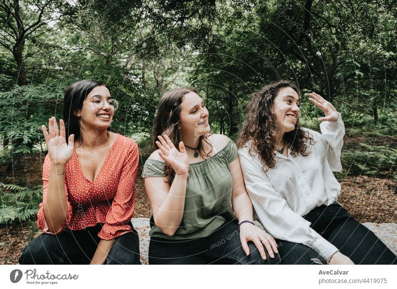 Three young woman saluting someone off camera in the forest, multicultural friendship concept, happiness concept student teenager women looking at camera