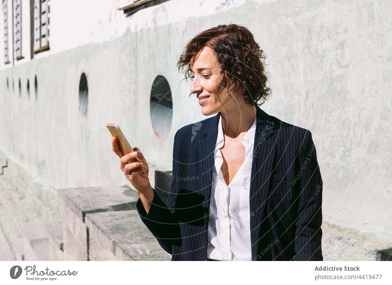 Smiling woman in formal wear browsing on smartphone executive using positive surfing business female connection professional device cellphone classy worker