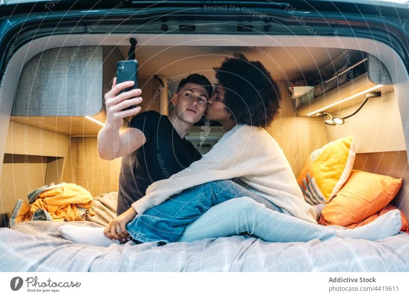 Happy couple taking selfie in camper van travel kiss love romantic together happy relationship young boyfriend girlfriend multiracial multiethnic diverse black