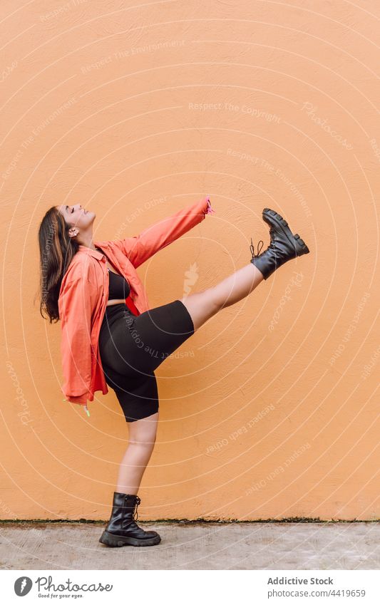 Energetic woman doing kick near painted wall cheerful move style posture cool fun dance energy female pleasure positive eyes closed trendy millennial delight