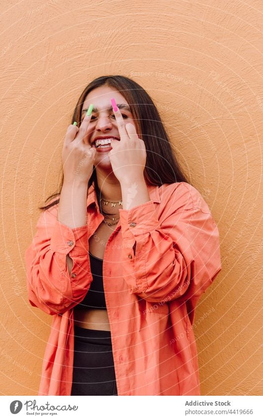Expressive woman showing fuck gesture against orange wall naughty provocative behavior laugh cool expressive female playful reaction middle finger rude