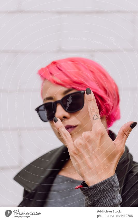 Woman with pink hair showing sign of horns woman gesture sunglasses style modern rock and roll brutal rebel bright hipster confident colorful cool female trendy