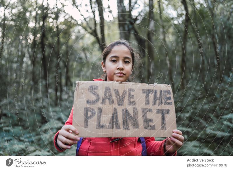 Ethnic girl with Save The Planet inscription on cardboard piece save the planet preserve nature environment ecology conserve forest portrait trunk tree support