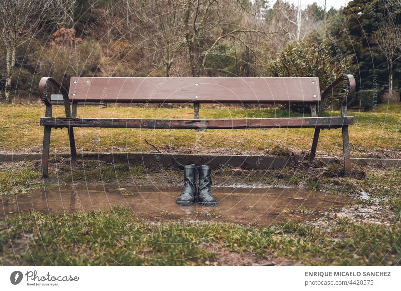 Boots next to park bench in the middle of a puddle, concept absence or loss of a loved one person boot shoe woman fashionable horizontal men togetherness ankle