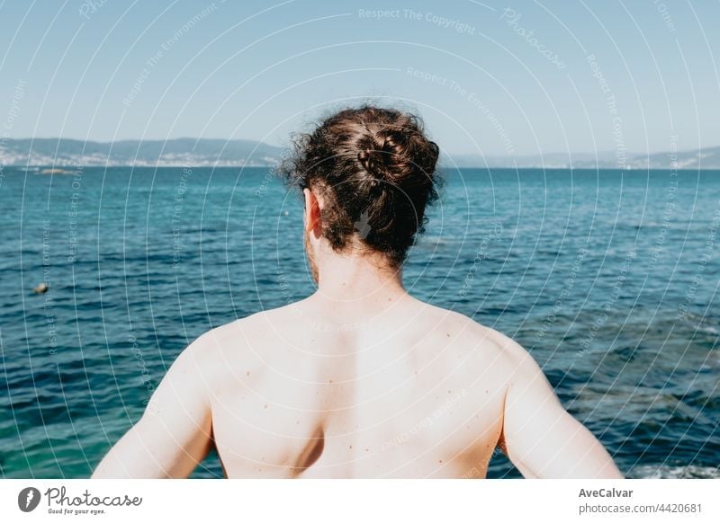 The back of a young man in front of the ocean during a sunny day with confidence, liberty and future concepts, copy space, summer, holiday horizontal standing