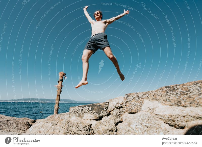 Young male with long hair jumping in the air, shirtless during a sunny day, space and liberty concept, holidays, fantastic image, beach day horizontal