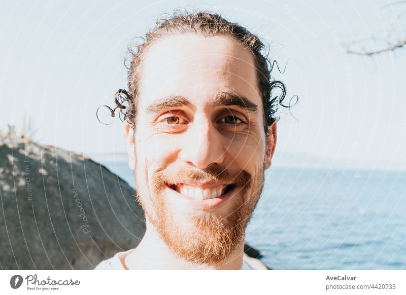 Super close up portrait of a young male with a blank white shirt smiling to camera in the coast of spain during a beach day, mental health happiness and future concept