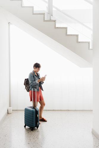 wide angle view of backpacker caucasian woman at train station using mobile phone app while waiting. Travel concept travel technology baggage internet online