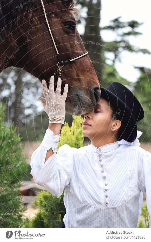 African American woman petting horse in countryside jockey elegant plant hat serious posture female black african american adult confident together lifestyle