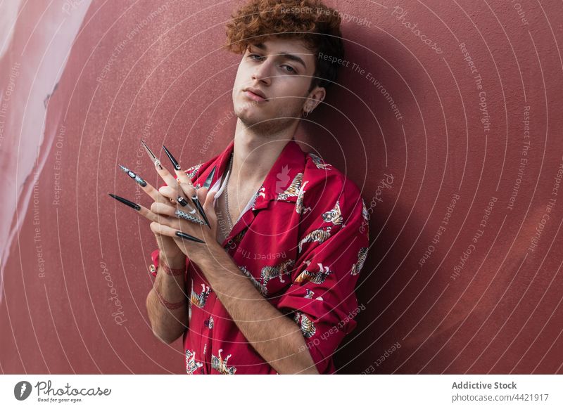 Cool gay model with false nails against wall homosexual manicure style fashion hands clasped individuality ignorant portrait creative design tattoo accept