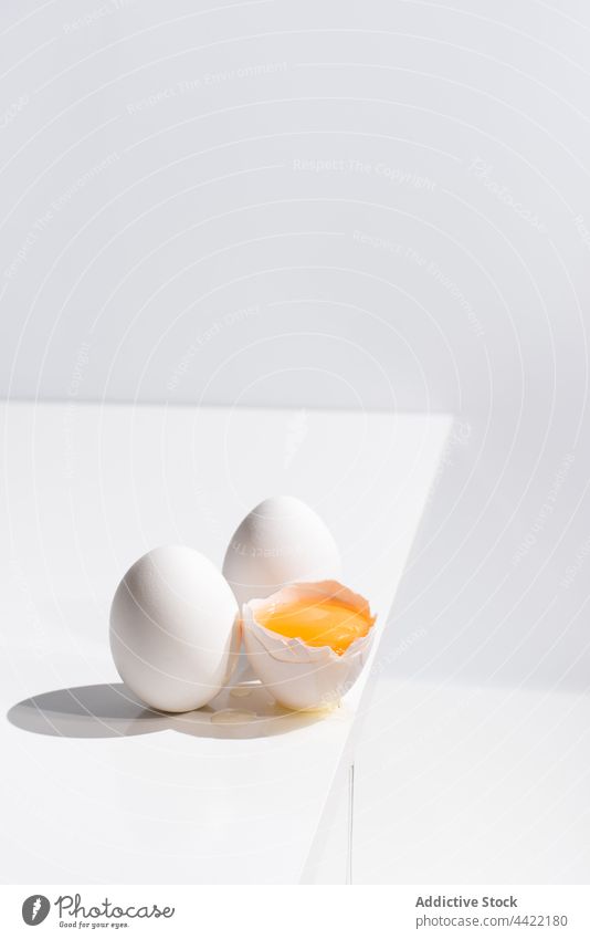 Whole and broken chicken eggs on white table yolk whole minimal color studio simple easter holiday fresh natural style food healthy shell nutrition plain desk