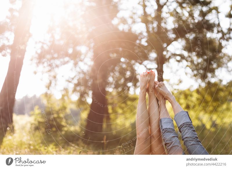 couple in love lying in the grass and lifting their legs up. summer sunny day feet young guy human two happiness happy spring woman together outdoors cheerful