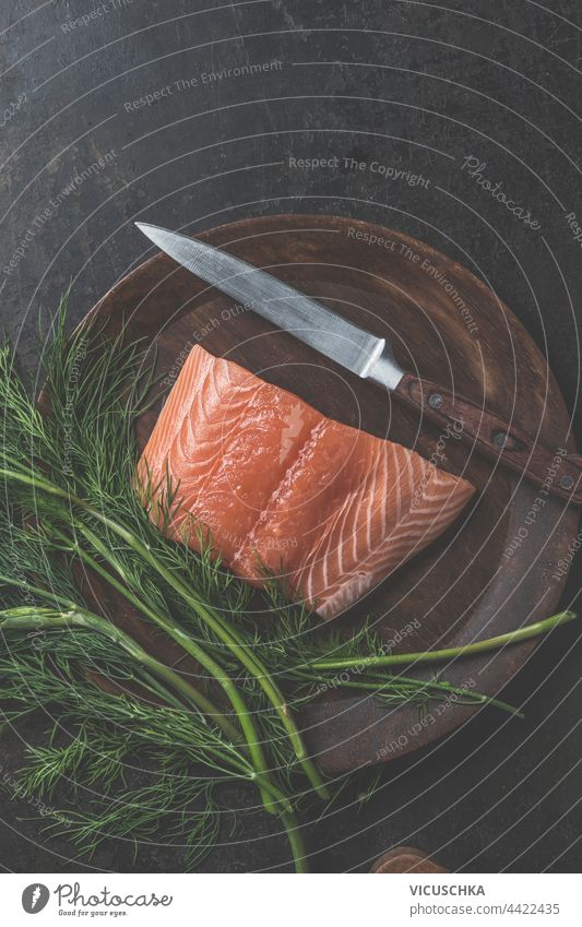 Portion of raw salmon fillet with a bunch of dill and a knife on a wooden plate. Top view portion top view above background cooking fish food fresh healthy