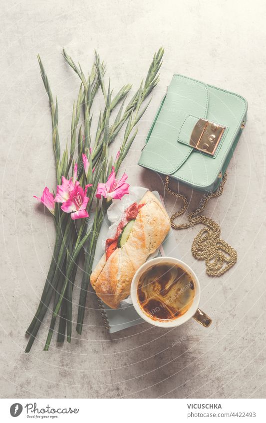 Cute aesthetic breakfast or lunch with coffee and sandwich, next to which there is a bouquet of flowers and a small women's handbag. Top view cute top view