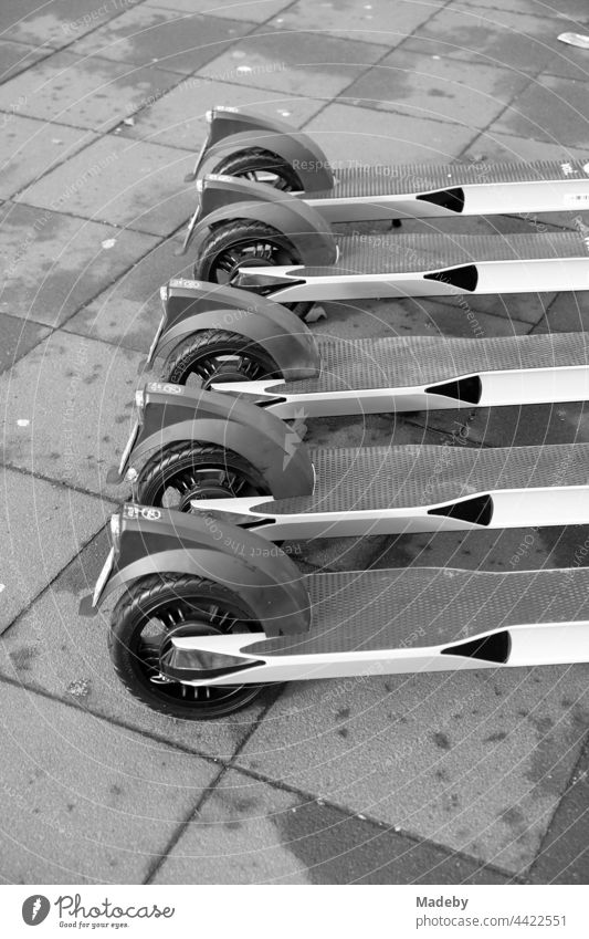 Controversial e-scooters for rent lined up on grey pavement in downtown Frankfurt am Main in Hesse, photographed in neo-realistic black and white e-roller