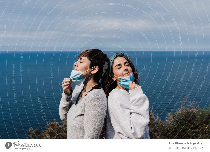 two caucasian women outdoors removing face mask, breathing and keeping social distance in Pandemic during corona virus. Nature and mountain woman nature sea